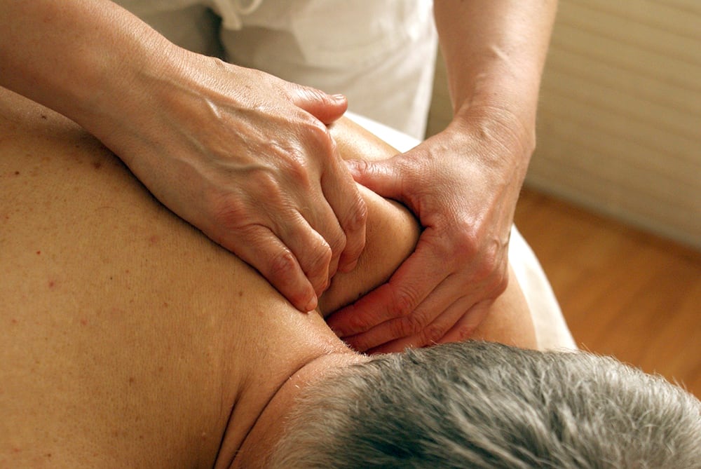 Close-up of strong hands massaging the shoulder area of an older grey-haired man